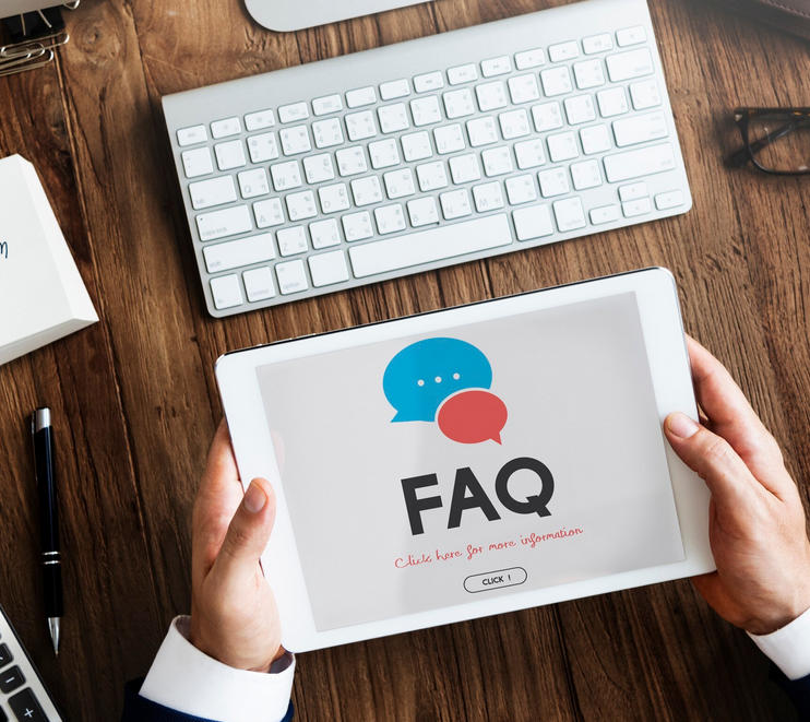 Hands holding a tablet showing FAQ on a desk